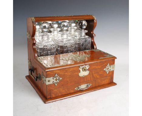 A late Victorian oak tantalus with silver plated mounts and bevelled mirror back, fitted with three cut glass decanters and s