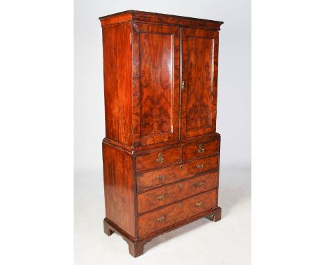 A George I walnut cabinet on chest, the moulded cornice above a pair of panelled cupboard doors, opening to a fitted interior
