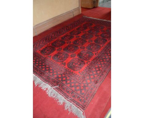 An Eastern carpet, 20th century, the madder ground with a rectangular field decorated with three rows of six octagonal shaped