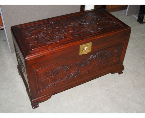 A Chinese camphor wood chest, late 19th/ early 20th century, the top and front panels carved with pairs of dragons contesting
