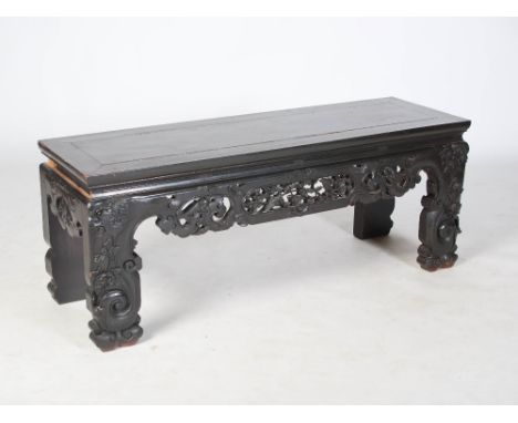 A Chinese dark wood low console table, 20th century, the panelled rectangular top above a pierced and carved apron centred wi