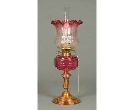A Victorian brass oil lamp, with ruby glass reservoir and etched glass shade.  Height including chimney 24 ins.  CONDITION RE