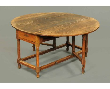 A George III oak gate leg table, oval in plan, raised on turned legs united by low moulded stretchers.  Width 57 ins, length 