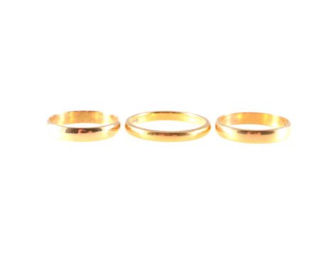 Three yellow metal wedding bands, two hallmarked 22 carat gold a 2.5mm wide plain D shape, ring size Q, a 3.3mm wide plain ha