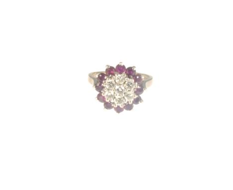 A circular ruby and diamond reverse cluster ring, seven brilliant cut diamonds claw set to centre and surrounded by a border 