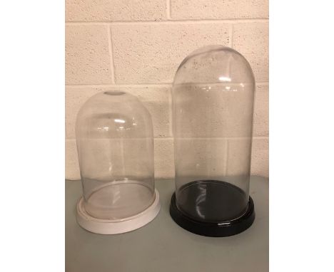 Glass display Domes, one approximately 50cm x 24cm with black ceramic base, and one approximately 38 x 24cm on a white cerami