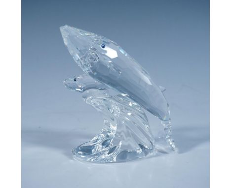 A clear faceted sculpture depicting a mother whale and her calf, both with blue eyes, riding the top of a wave. 1992 Swarovsk
