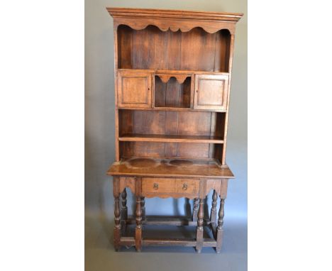 An Oak Dresser, the moulded cornice above a boarded shelf back with two cupboards, the lower section with a central drawer ra