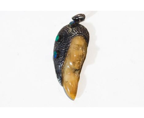 An opal, bone and white metal mounted pendant, carved as the face of a female, inset with three opals to the hair, 6 cm long