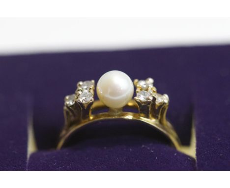 A cultured pearl and diamond ring, stamped '18K', the pearl, of approximately 5.5 mm diameter, flanked either side by a trio 
