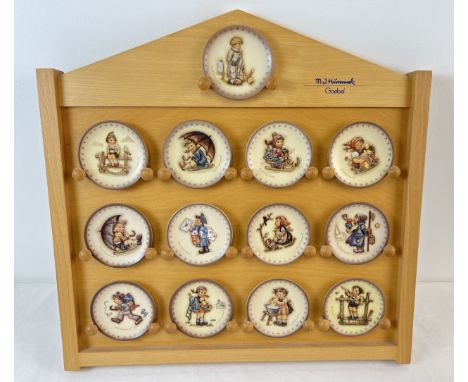 A collection of 13 assorted M.J. Hummel Goebel ceramic miniature plates together with a wooden wall display stand. 11 boxed a