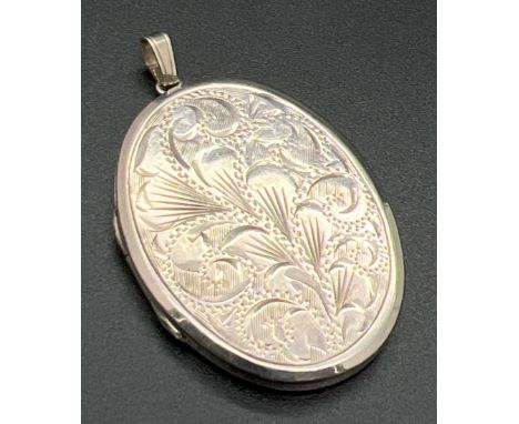 A large vintage silver oval shaped locket with floral engraving to front and engine turned decoration to back. Silver marks t