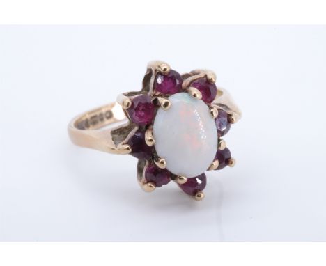 An opal and ruby dress ring, comprising an oval opal cabochon of approx 8 mm x 6 mm framed by eight small round-cut garnets o