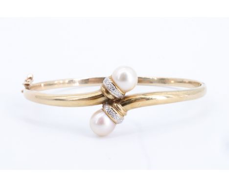 A 9 ct gold, pearl, and diamond hinged bangle, of faux torque form, its terminals set with 8 mm pearls on precious white meta