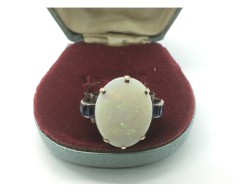 An unmarked large opal ring flanked by blue sapphires, approx size V-W.