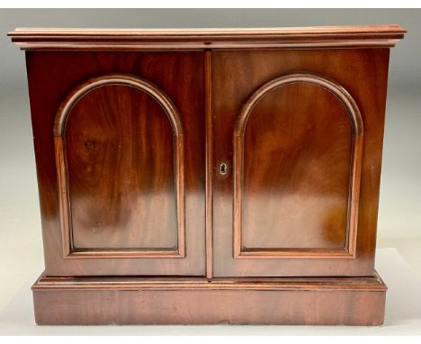 A Victorian mahogany table top collector's cabinet, oversailing top above a pair of arched panelled doors enclosing two rows 