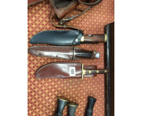 Three various hunting knives in leather sheaths.