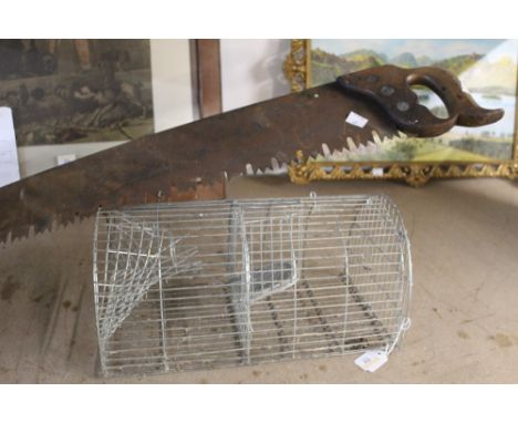 A metal animal trap together with a vintage saw