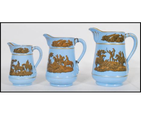 A group of three 19th Century graduating prattware pitcher jugs having blue grounds with transfer printed golden yellow hunti