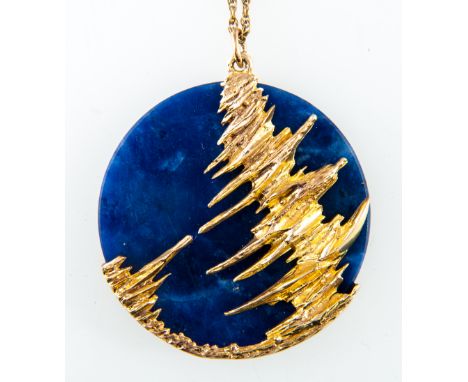 A lapis lazuli pendant and chain, the oval disc of Lapis 50mm diameter is set in a yellow metal modern abstract mount of a te