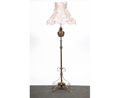 An Arts and Crafts brass standard oil lamp, adapted for electricity, reservoir fitted within a scroll basket, tripod base wit