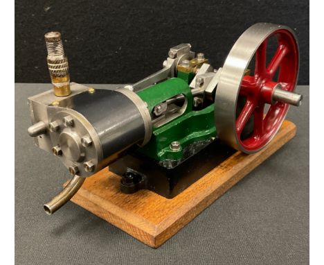 A Stuart single cylinder stationary live steam engine. Horizontal engine with 130mm flywheel. Mounted on oak base and painted