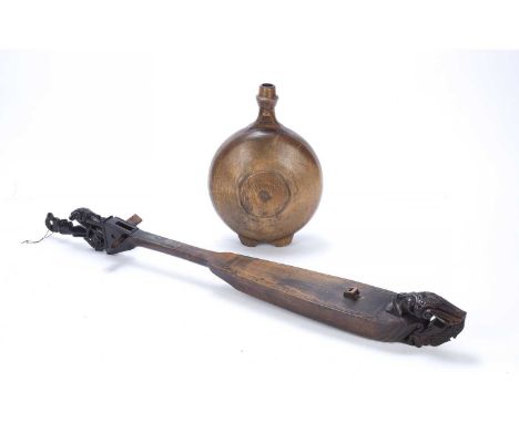 An Indonesian lute, carved wood of boat shape with a seated figure finial, 77cm long and a wooded water container (2) Provena