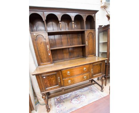 An early 20th century oak dresser, the upper section with an arcaded shelf over two doors and a central plate rack, the base 