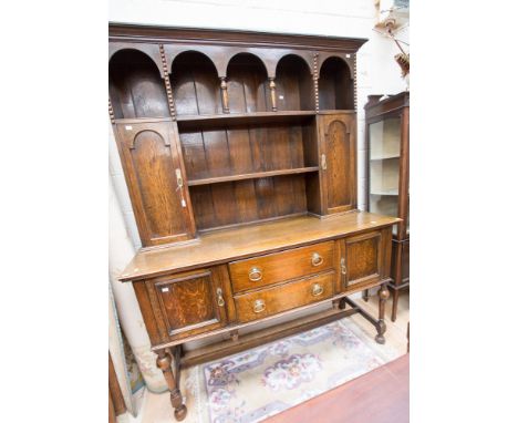 An early 20th century oak dresser, the upper section with an arcaded shelf over two doors and a central plate rack, the base 