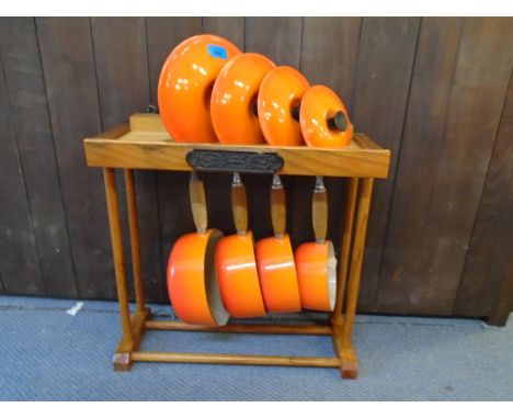 A Le Crueset pan set with original pine wooden stand comprising four graduated saucepans and lids with teck handles in an ora