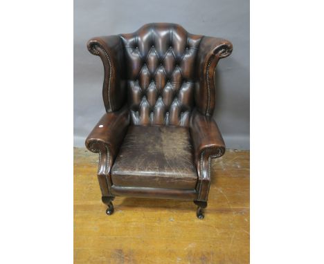 A BROWN LEATHER UPHOLSTERED WING BACK ARMCHAIR, the button upholstered back with overstuffed arms brass studding loose cushio