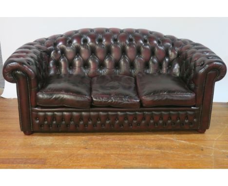 A WINE LEATHER UPHOLSTERED CHESTERFIELD STYLE SOFA, the buttoned upholstered back and sides with loose cushions on bun feet,1