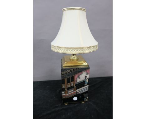 AN ORIENTAL STYLE TABLE LAMP, the cream shade above a rectangular base decorated with figures and street scenes, on brass bun