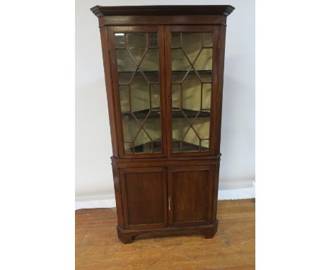 A GEORGIAN STYLE MAHOGANY CORNER CABINET the moulded corners above a plain frieze the pair of astragal glazed doors revealing