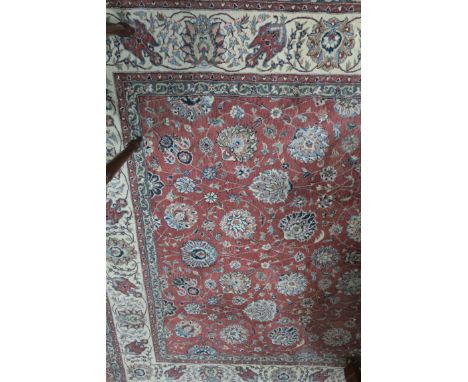 A RECTANGULAR WOOL RUG the rose coloured central panel filled with flower heads and trailing foliates with a conforming beige