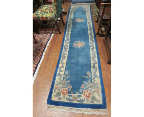 A CHINESE WOOL RUNNER, the blue and white ground with central floral panel within a conforming border,346cms x 72cms.