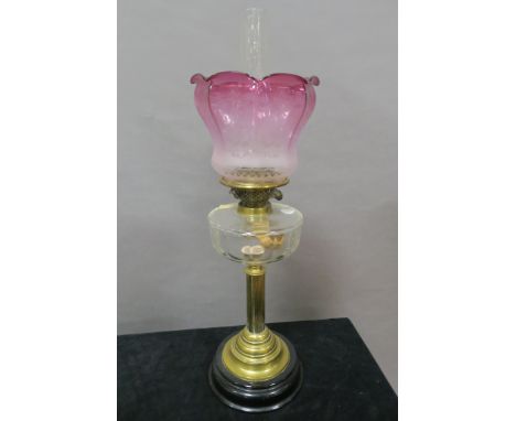 A VICTORIAN BRASS FRAMED AND GLASS MOUNTED OIL LAMP, the flared ruby and clear glass etched shade above a plain reservoir on 