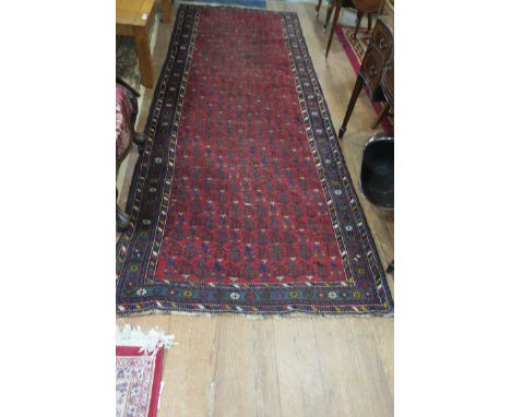 AN ANTIQUE PERSIAN KURDISH WOOL RUNNER, the wine ground with central panel within a conforming border,338cms x 125cms.