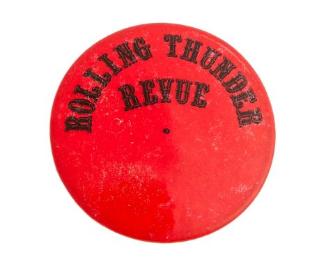 A red round lapel button with the Rolling Thunder Revue logo in black letters across the top and a mostly smoked joint tucked