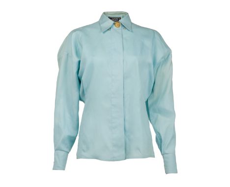 A pale blue cotton dress shirt, owned by Elizabeth Taylor. The shirt has a gold tone button embossed with the Versace Medusa 