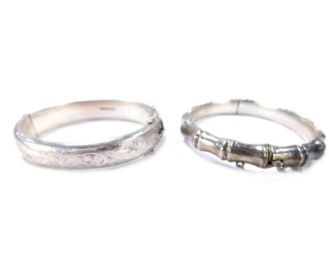 Two silver bangles, comprising a Victorian half hinged foliate scroll bangle, with safety chain, and another of shaped form, 