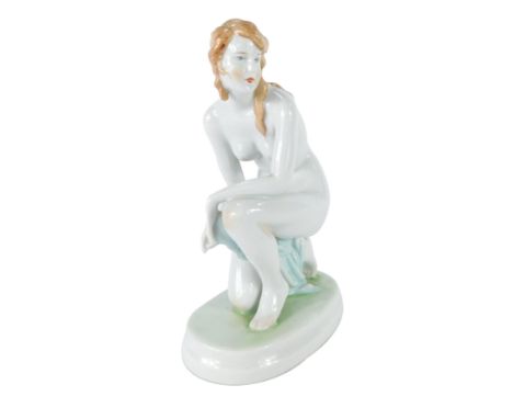 A 20thC Zsolnay Pecs porcelain figure, modeled as a naked kneeling woman, on an oval base, printed mark, 22cm high.