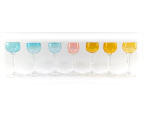 A set of seven coloured wine glasses, three blue, three green and one pink, on a clear glass stem with frilled knop, etched t