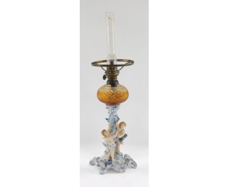 A Continental porcelain cherub oil lamp, the amber glass faceted reservoir on a blue and white porcelain stem with two cherub