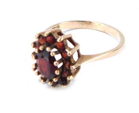 A 9ct gold garnet cluster ring, with large oval garnet surrounded by a row of smaller stones in a raised basket setting, size