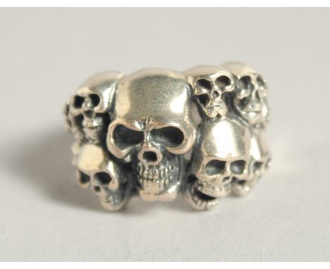 A SILVER RING WITH TEN SKULLS.