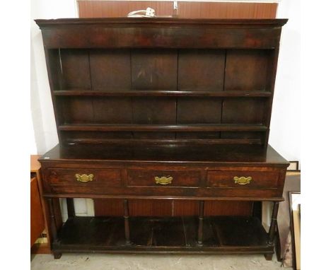 An 18th century provincial Welsh oak dresser having an open plate rack over three drawers with brass handles, turned legs, un