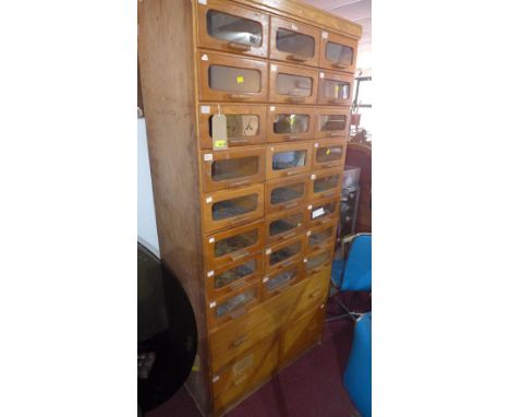 An early to mid 20th century light oak Haberdashery cabinet with 24 glass fronted drawers, above two long drawers raised on p