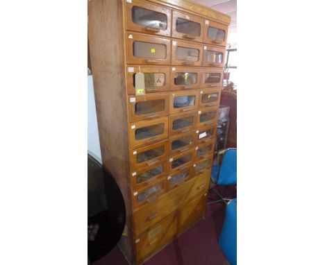 An early to mid 20th century light oak Haberdashery cabinet with 24 glass fronted drawers, above two long drawers raised on p