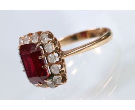 Synthetic ruby and white stone cluster ring. The ring being set with a rectangular step cut synthetic ruby with a halo of rou